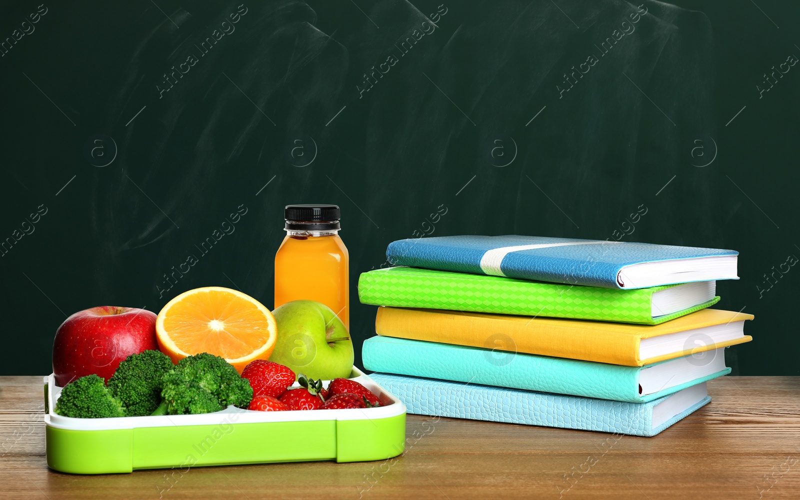 Image of Tray with healthy food and notebooks on wooden table near green chalkboard. School lunch