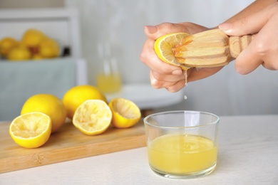 Woman squeezing lemon juice with reamer at white wooden table, closeup. Space for text