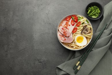 Photo of Delicious ramen in bowl served on grey textured table, flat lay and space for text. Noodle soup