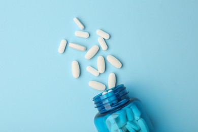 Photo of Vitamin pills and bottle on light blue background, top view