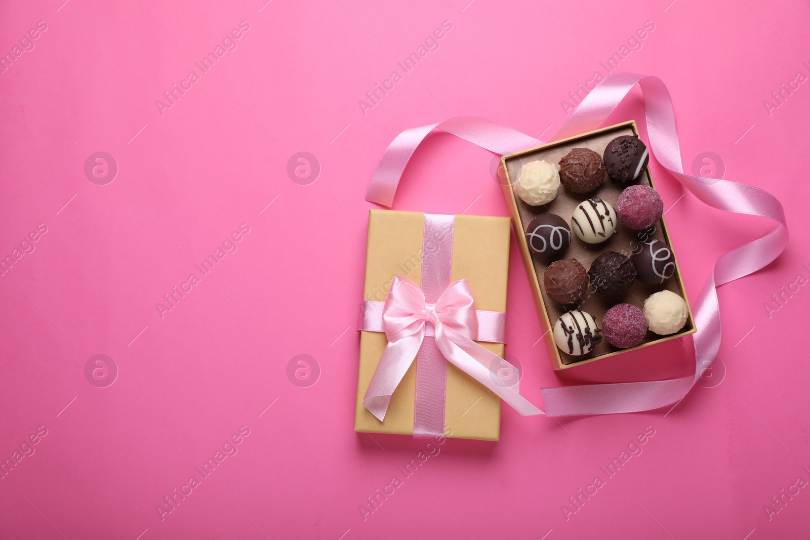 Photo of Open box with delicious chocolate candies and ribbon on pink background, top view. Space for text