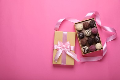 Open box with delicious chocolate candies and ribbon on pink background, top view. Space for text