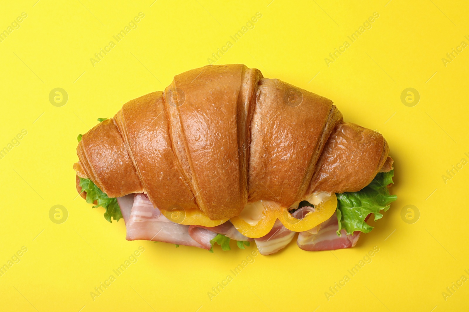 Photo of Tasty croissant sandwich with ham on yellow background, top view