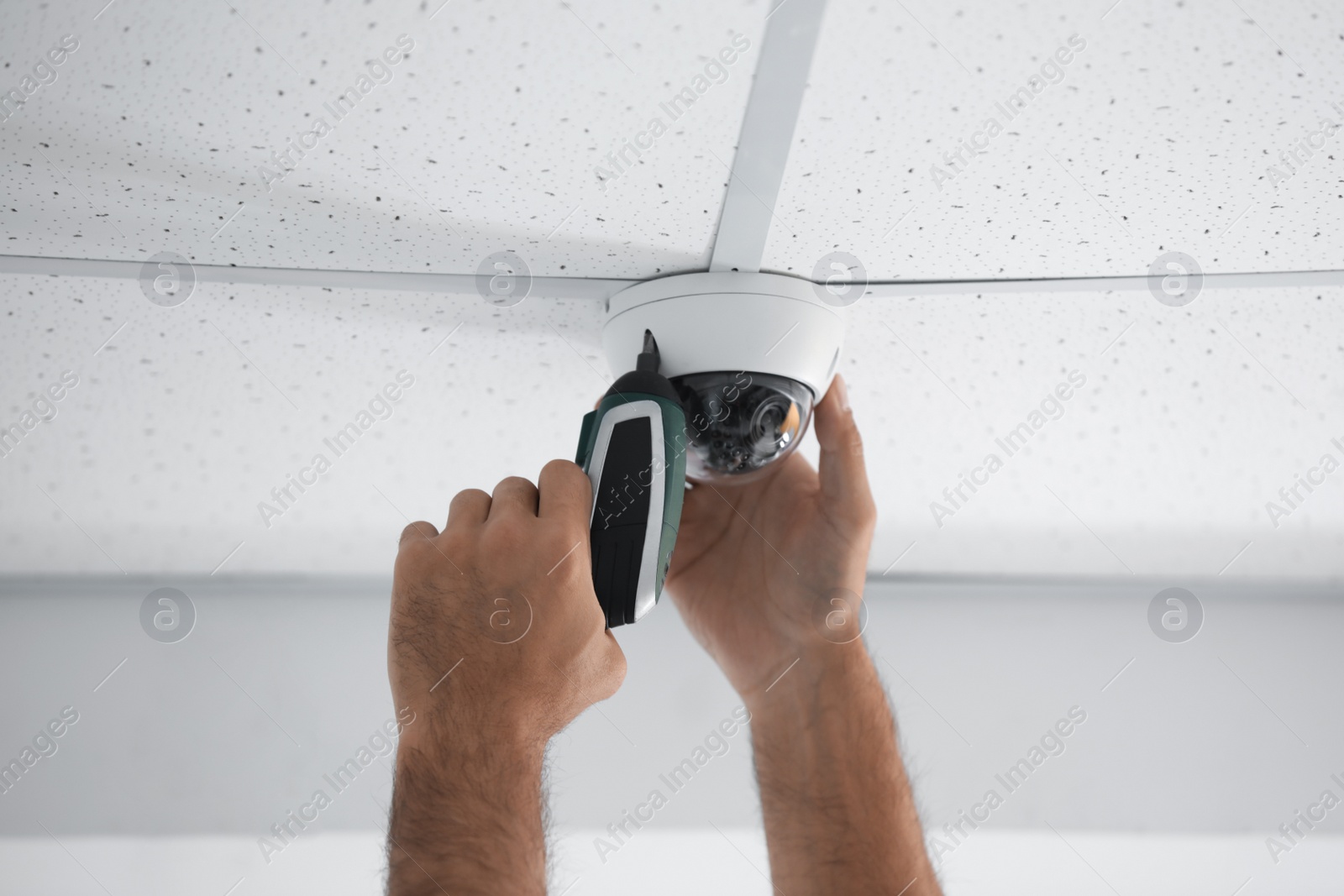 Photo of Technician installing CCTV camera on ceiling indoors, closeup