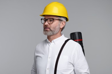 Photo of Architect in hard hat with drawing tube on grey background