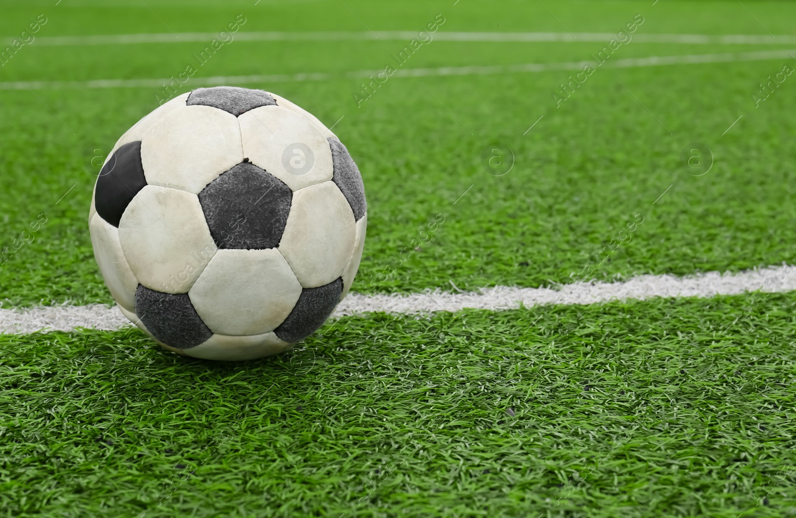 Photo of Dirty soccer ball on green football field, space for text