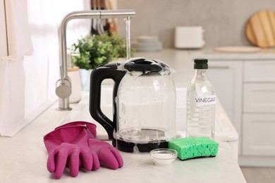 Photo of Cleaning electric kettle. Bottle of vinegar, sponge, rubber gloves and baking soda on countertop in kitchen
