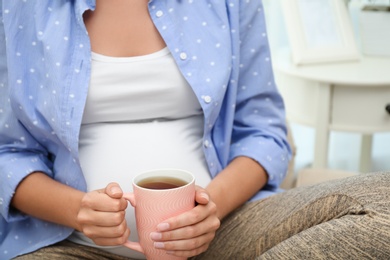 Pregnant woman drinking tea at home, closeup