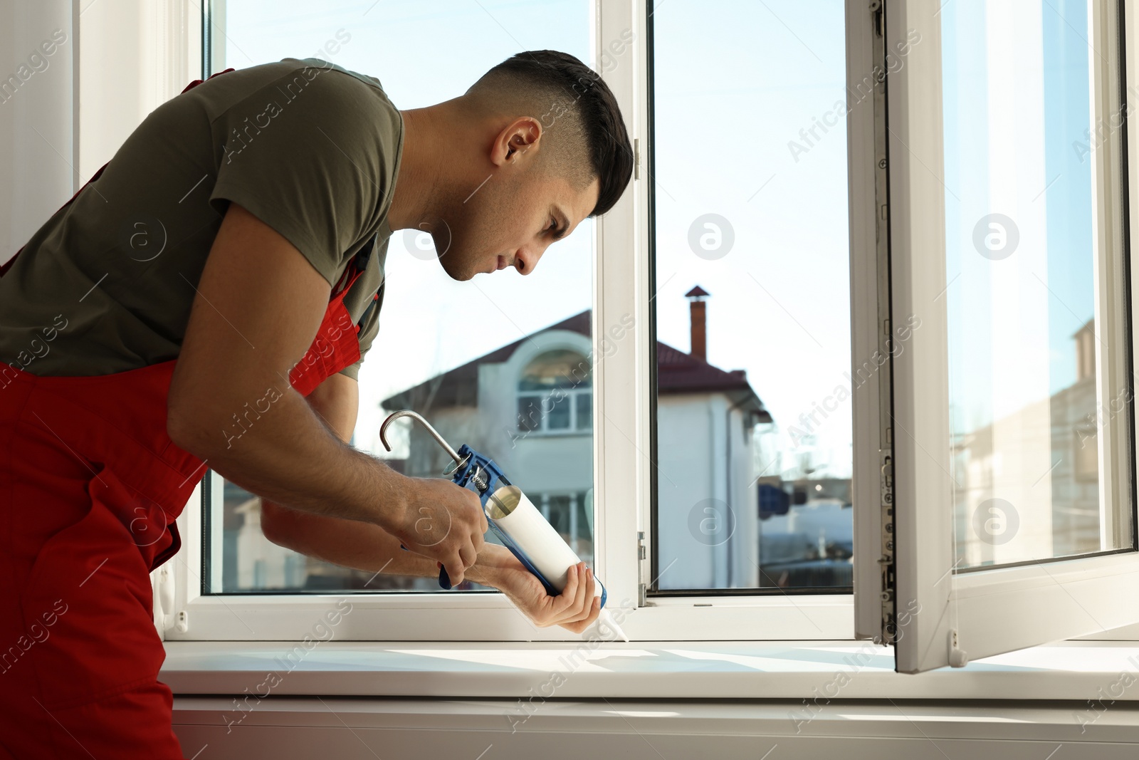 Photo of Construction worker sealing window with caulk indoors
