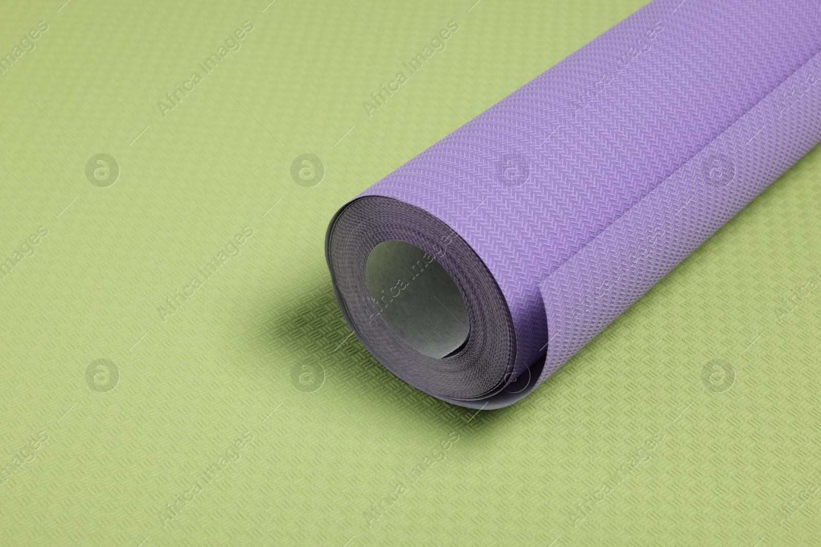 Photo of One violet wallpaper roll on green sample, space for text