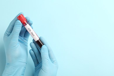 Photo of Scientist holding tube with blood sample and label STD Test on light blue background, top view. Space for text