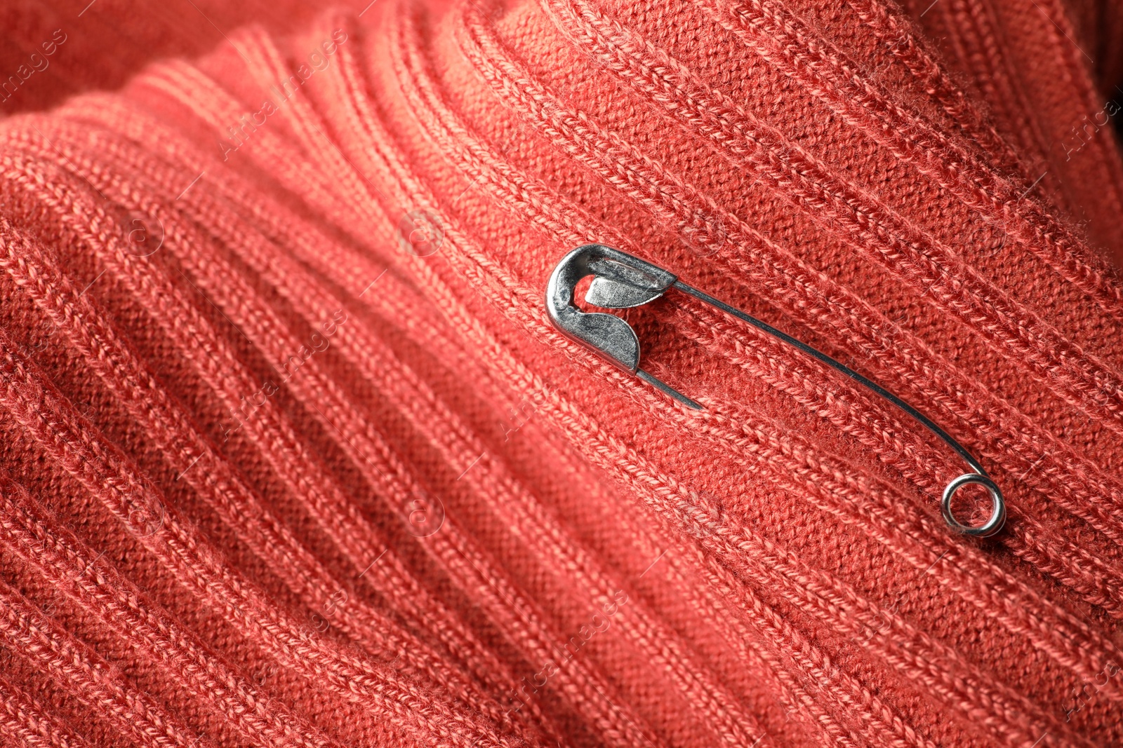 Photo of Metal safety pin on coral fabric, closeup