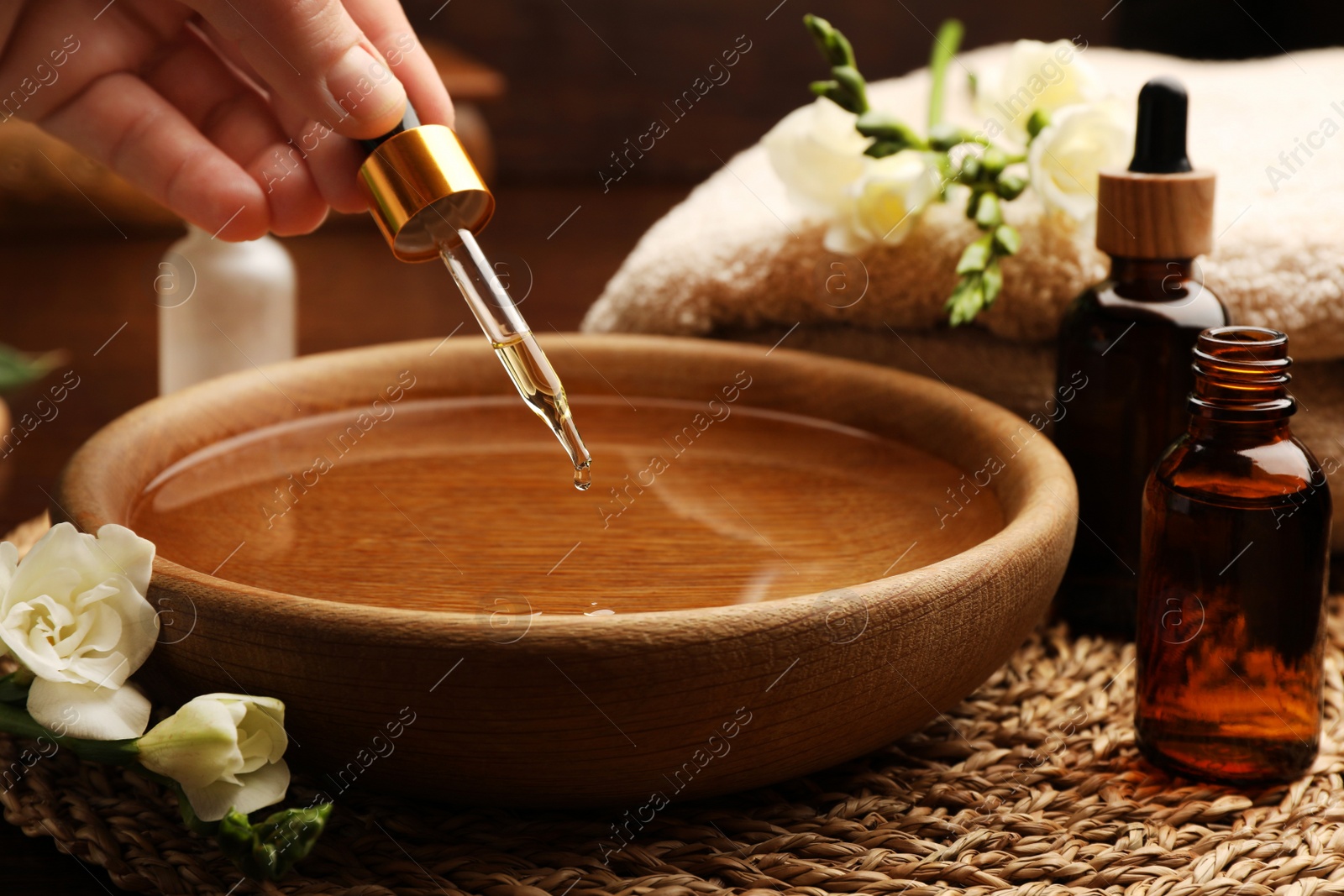 Photo of Woman dripping essential oil into bowl at table, closeup. Aromatherapy treatment