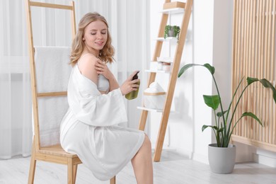 Photo of Beautiful young woman applying oil onto shoulder indoors