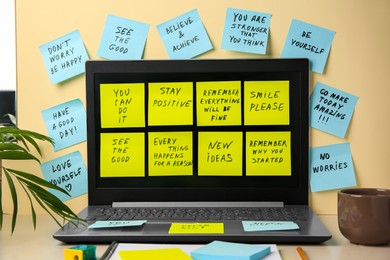 Photo of Paper notes with life-affirming phrases and laptop on table against beige background