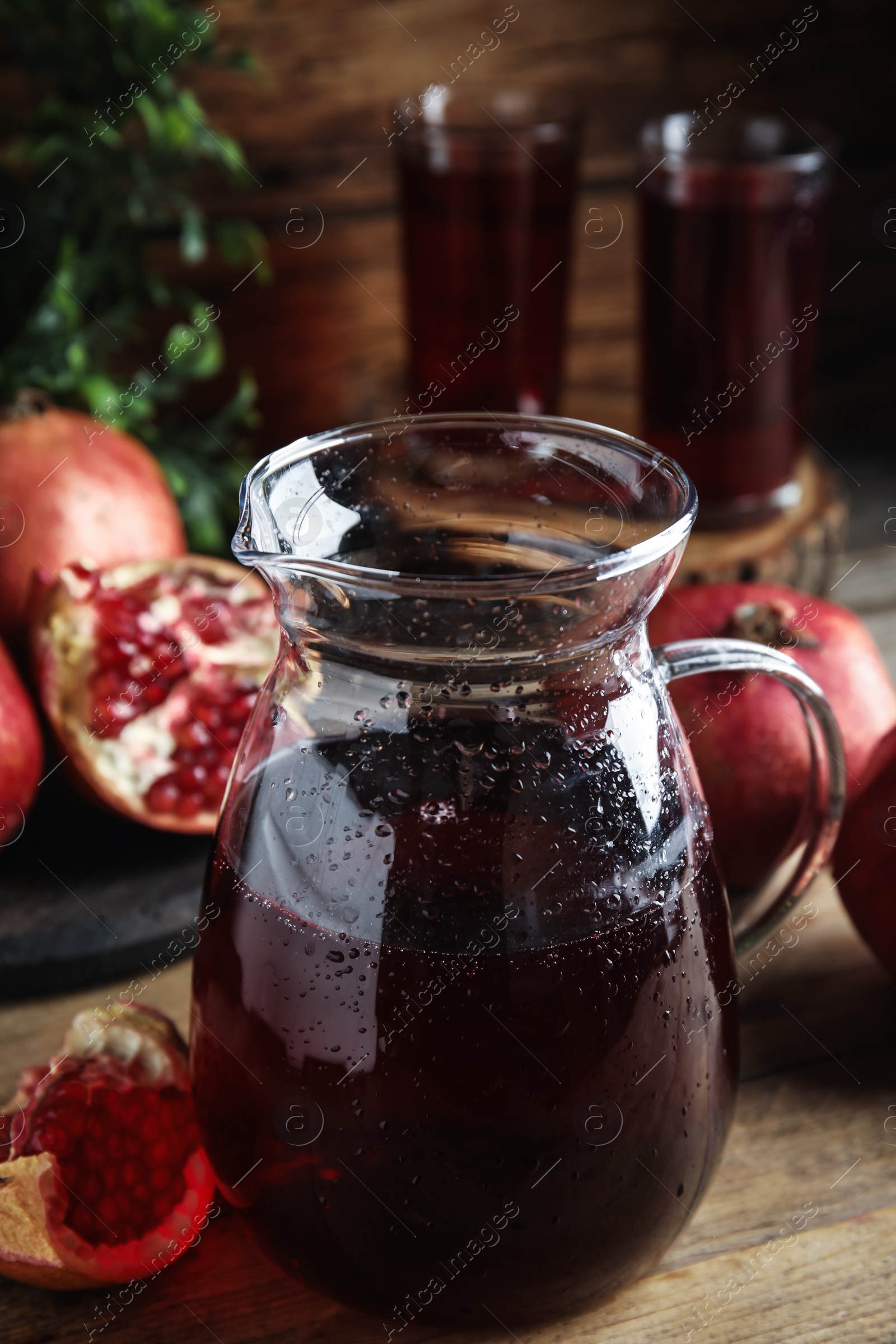 Photo of Jug of pomegranate juice and fresh fruits on wooden table