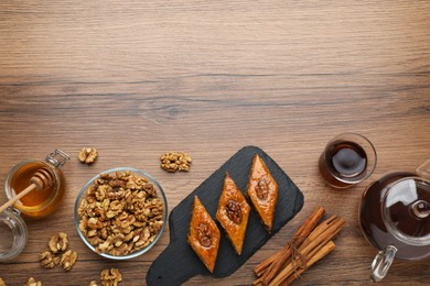 Photo of Delicious sweet baklava with walnuts, honey, cinnamon and hot tea on wooden table, flat lay. Space for text