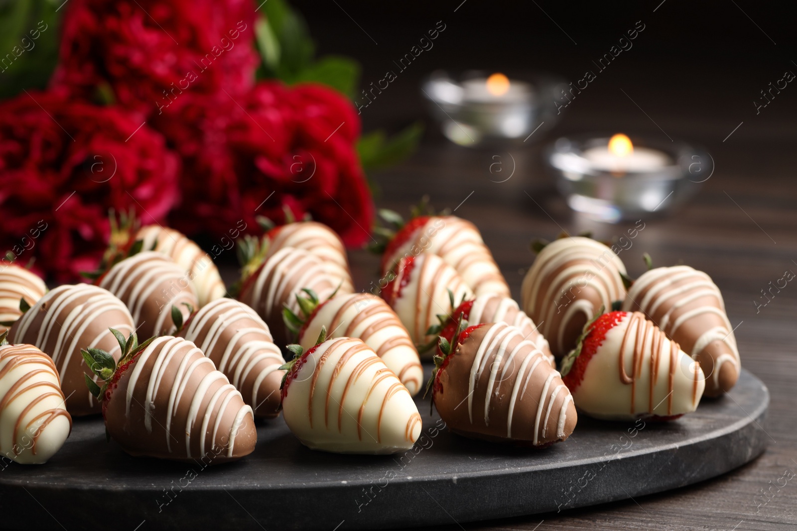 Photo of Delicious chocolate covered strawberries, flowers and burning candles on wooden table, closeup