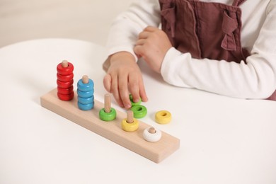 Photo of Little girl playing with stacking and counting game at white table indoors, closeup. Child's toy