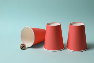 Photo of Three red cups and dice on light blue background. Thimblerig game