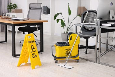 Photo of Cleaning service. Mop, wet floor sign and bucket in office