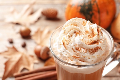 Photo of Glass cup with tasty pumpkin spice latte on wooden table, closeup