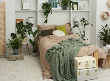 Stylish bedroom with comfortable bed and different houseplants. Interior design