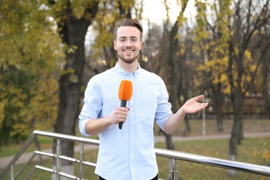 Photo of Young male journalist with microphone working in park
