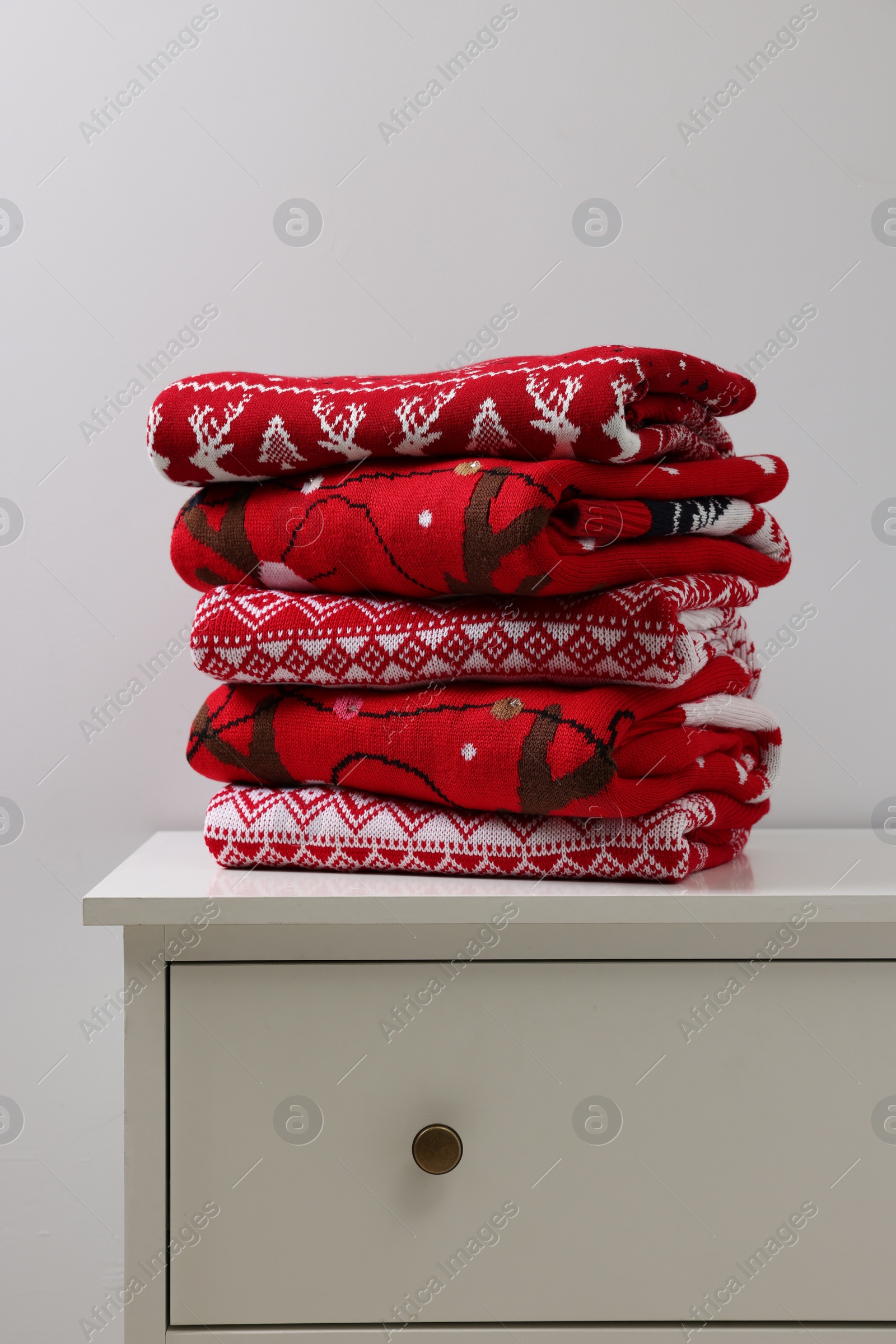 Photo of Different folded Christmas sweaters on chest of drawers against light background