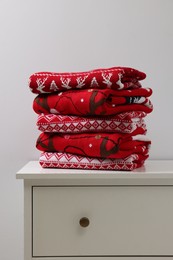 Different folded Christmas sweaters on chest of drawers against light background