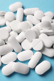 Photo of Pile of white pills on light blue background, above view