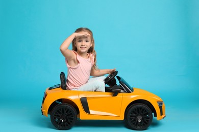 Photo of Cute little girl driving children's electric toy car on light blue background