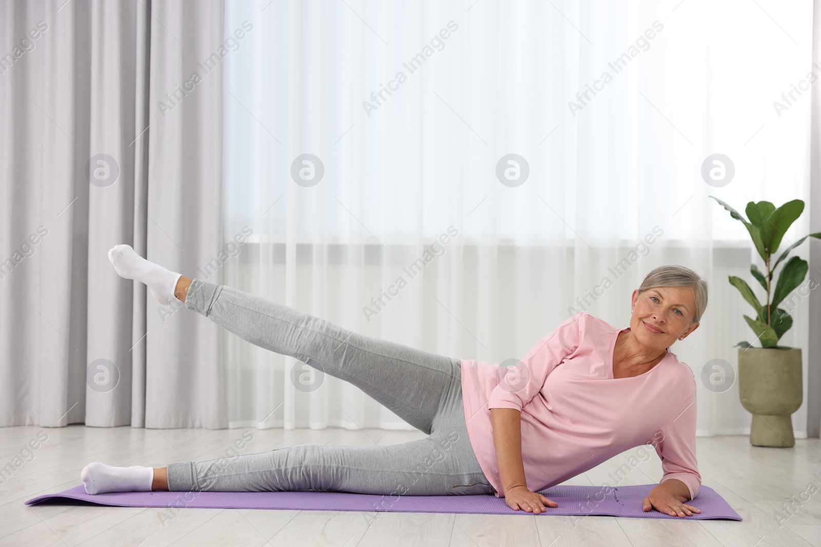 Photo of Happy senior woman practicing yoga on mat at home