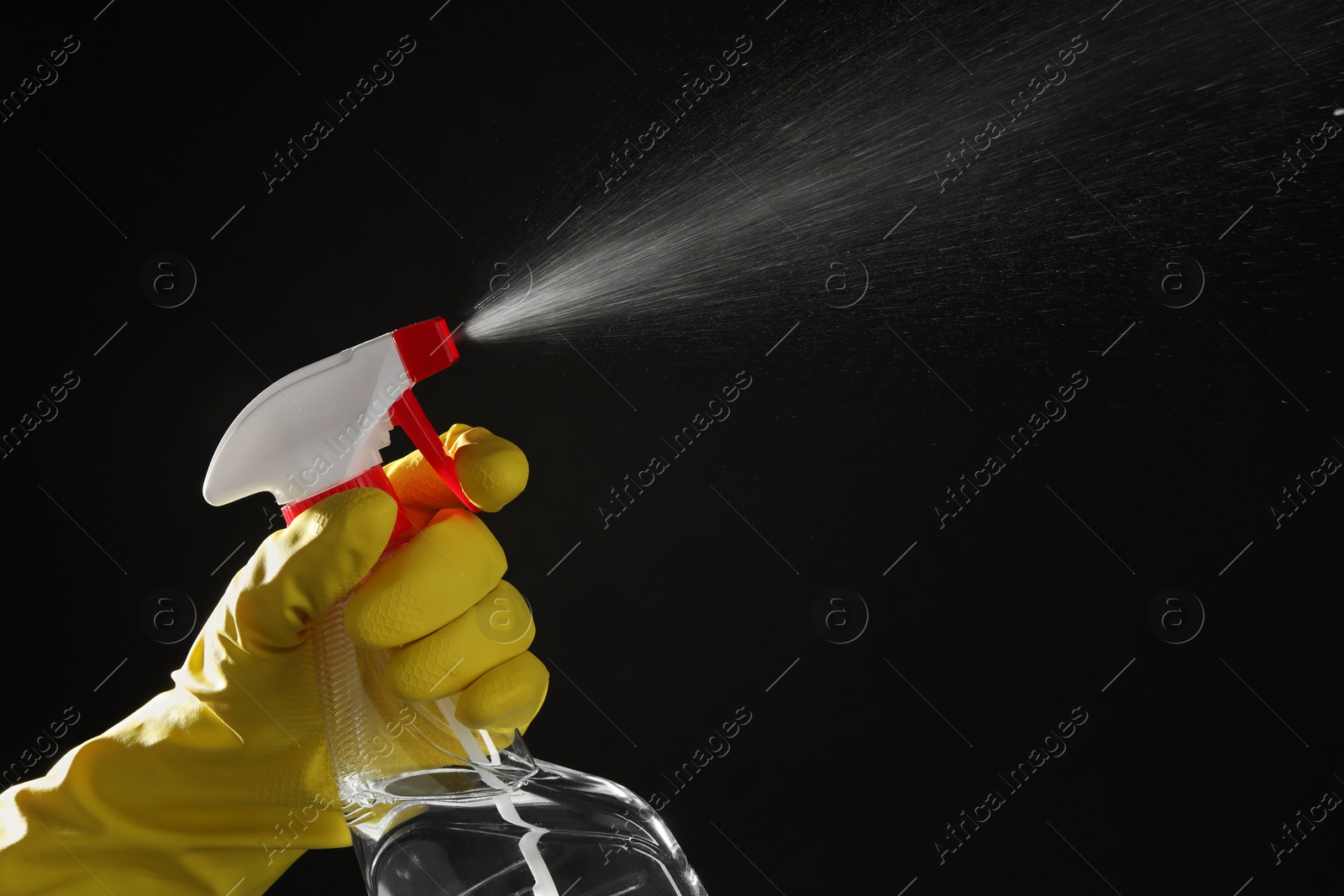 Photo of Woman spraying liquid from bottle on black background, closeup