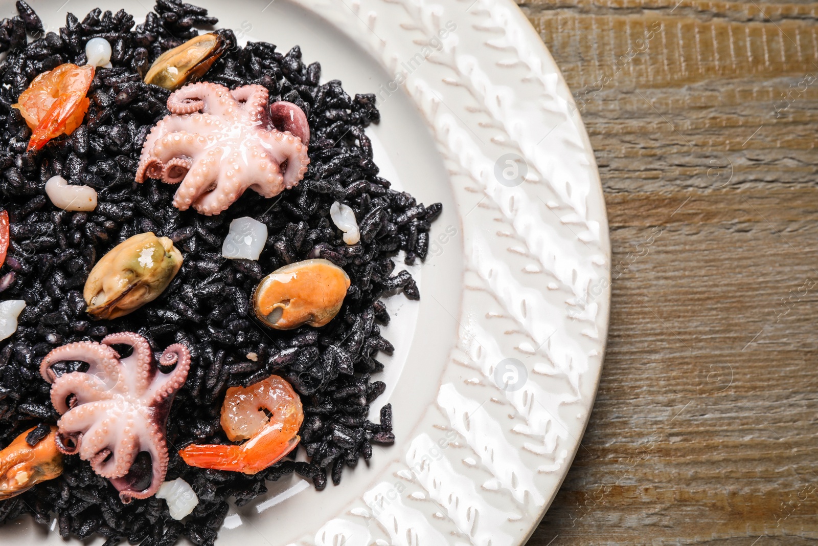 Photo of Delicious black risotto with seafood served on plate, top view