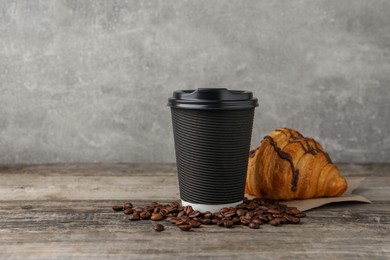 Photo of Coffee to go. Paper cup with tasty drink, croissant and beans on wooden table. Space for text