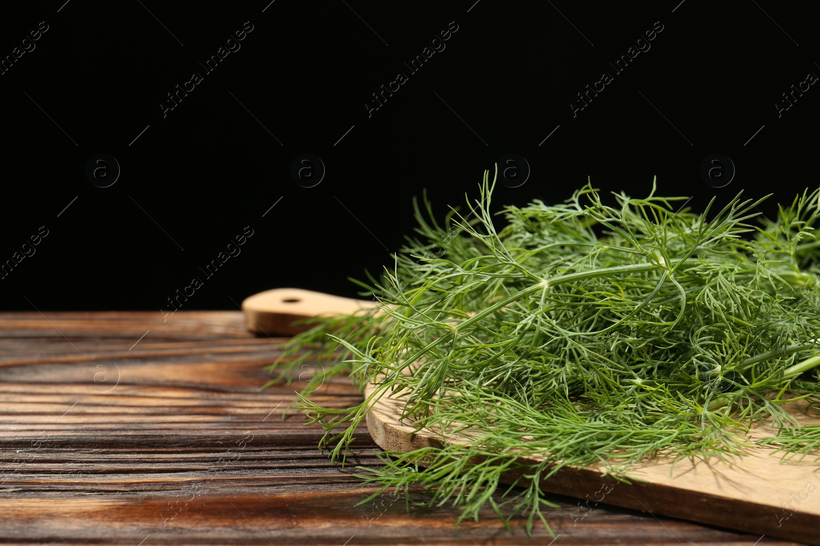 Photo of Board with fresh green dill on wooden table against black background, closeup. Space for text
