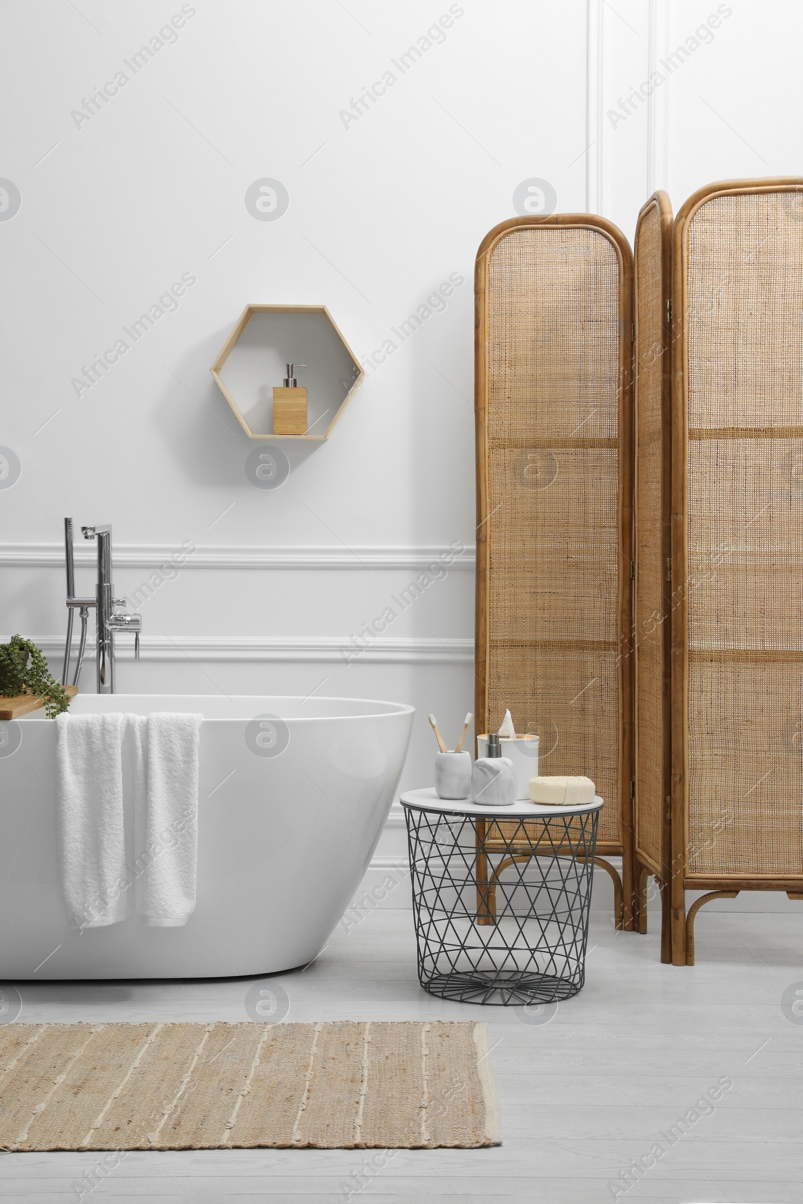 Photo of Modern ceramic bathtub and table with toiletries near white wall in room