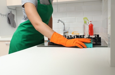 Photo of Woman cleaning gas stove with sponge in kitchen