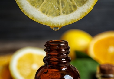 Photo of Citrus essential oil dripping from lemon slice into bottle, closeup
