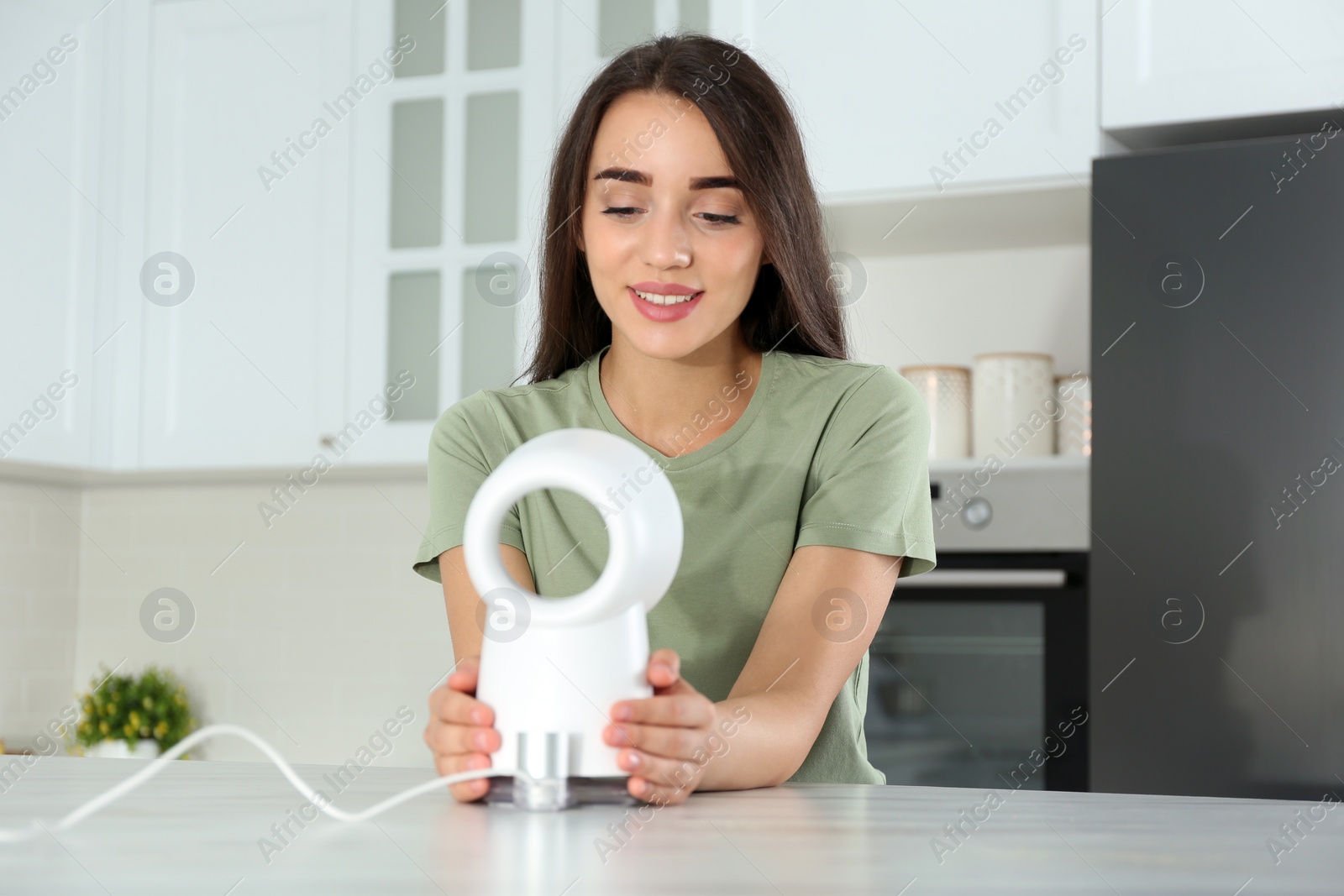 Photo of Woman enjoying air flow from portable fan in kitchen. Summer heat