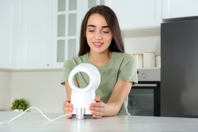 Woman enjoying air flow from portable fan in kitchen. Summer heat