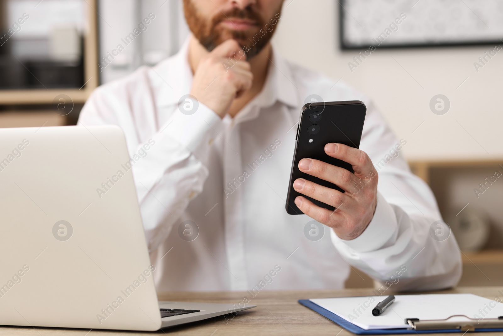 Photo of Man using smartphone at table in office, closeup