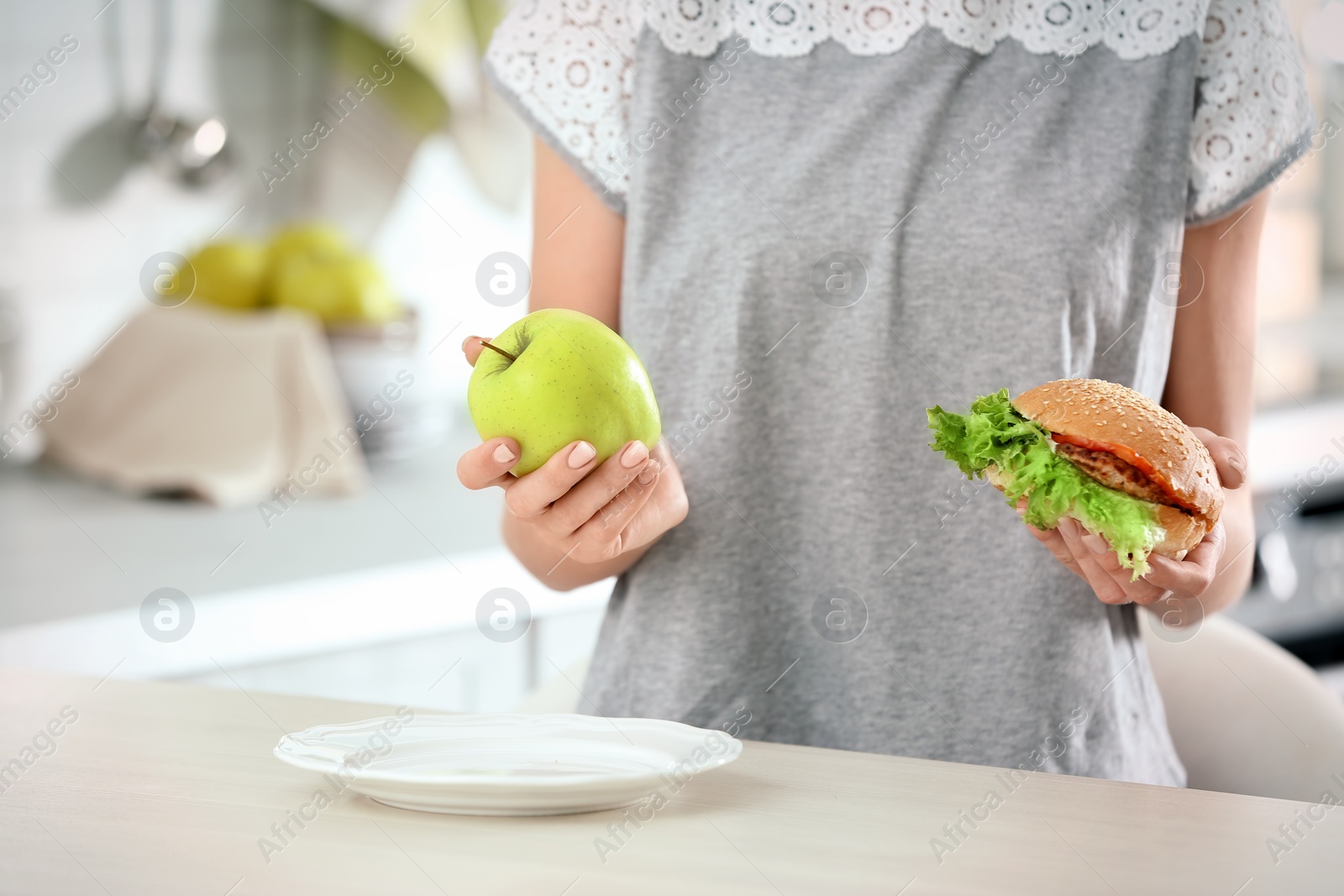 Photo of Woman holding tasty sandwich and fresh apple over table. Choice between diet and unhealthy food