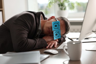 Man with fake eyes painted on sticky notes snoozing at workplace in office