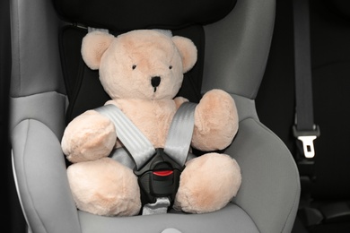 Photo of Teddy bear in child safety seat inside car. Danger prevention