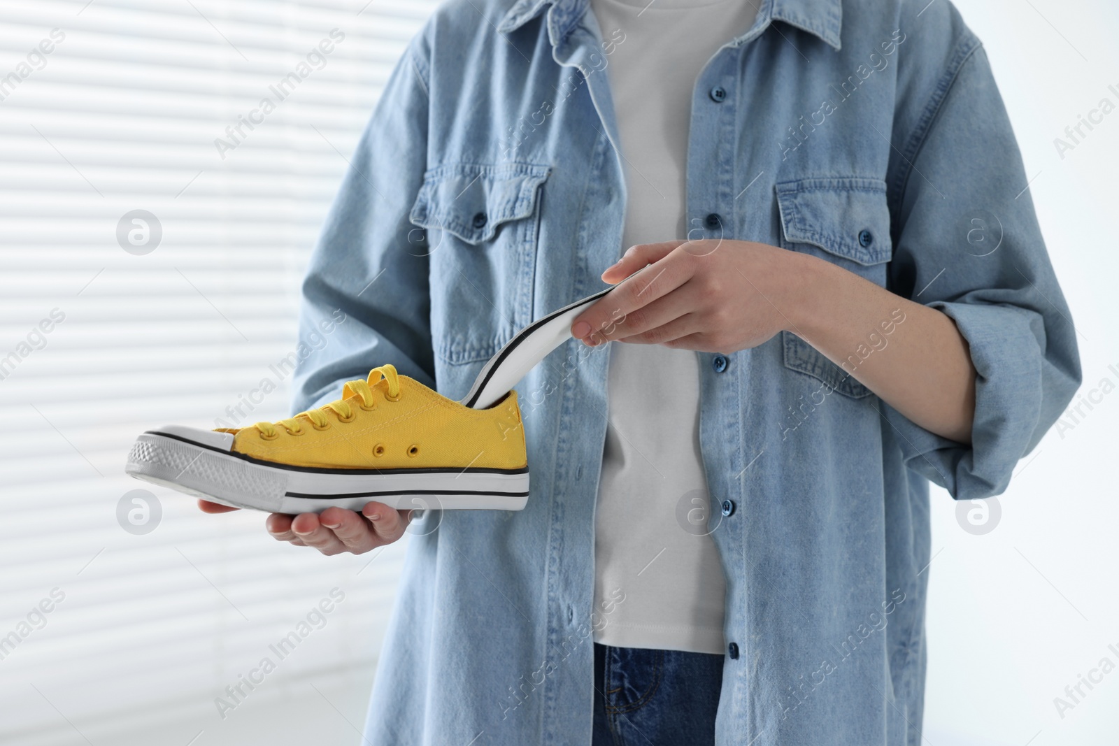 Photo of Woman putting orthopedic insole into shoe indoors, closeup. Foot care