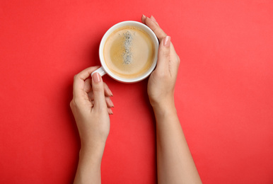 Woman with cup of coffee on red background, top view