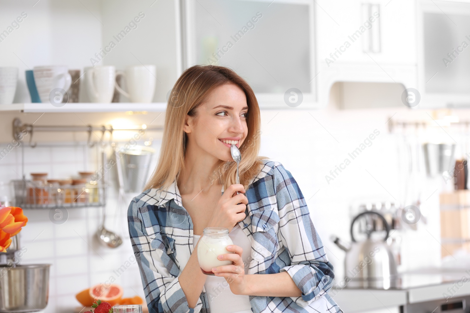 Photo of Young attractive woman eating tasty yogurt in kitchen