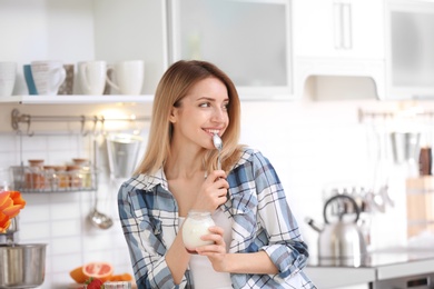 Young attractive woman eating tasty yogurt in kitchen